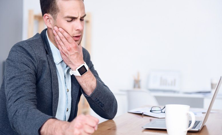 Man experiencing T M J dysfunction holding jaw in pain