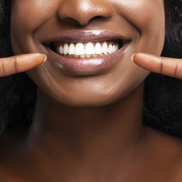 Woman pointing to healthy smile after tooth extractions