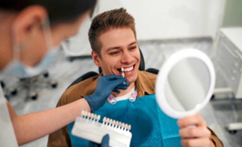 Patient smiling at reflection in dental mirror during veneers consultation