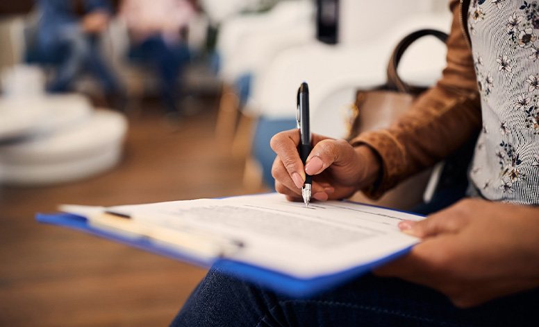 Woman’s hands filling out forms on blue clipboard.