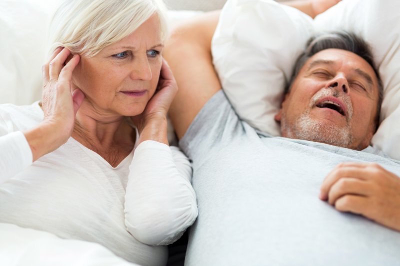 Older man snoring, woman covering her ears