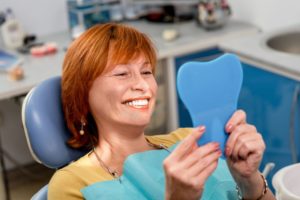 a woman at the dentist smiling at her dentures in mirror