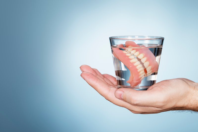 Hand holding water glass with dentures in them