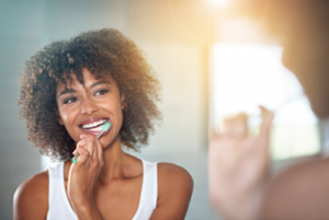Woman brushing her teeth in bathroom mirror