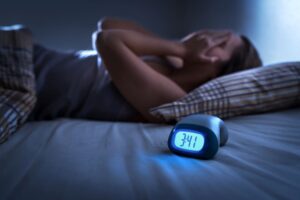 Woman in bed with hands over face next to digital clock displaying 3:41